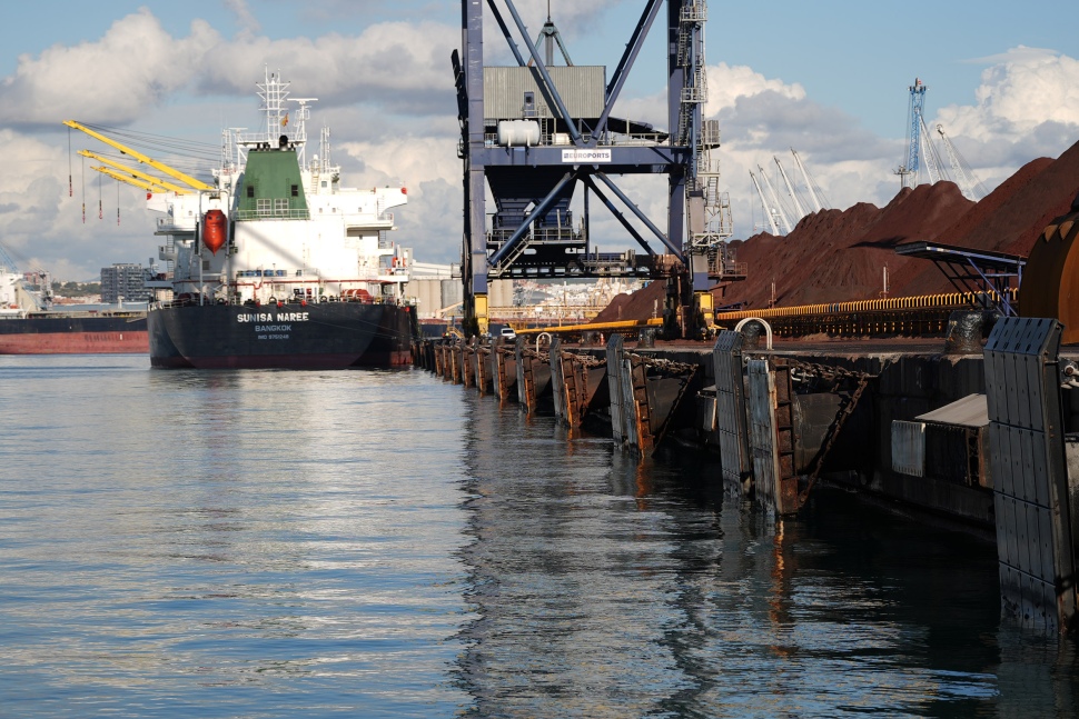 El puerto de Tarragona adapta el muelle de Cataluña para recibir barcos más grandes con mineral de hierro  El Puerto de Tarragona está realizando mejoras en el muelle de Cataluña para poder recibir barcos de carga de mayor tamaño, dedicados al tráfico de mineral de hierro. Con una inversión de 2,1 millones de euros, el proyecto tiene como objetivo modernizar la infraestructura portuaria para dar respuesta a las nuevas necesidades derivadas de este tráfico.  El principal componente de este proyecto será la instalación de 28 defensas marítimas, diseñadas para absorber el impacto de los grandes barcos previstos. Las defensas actuales, instaladas en 2015, necesitan ser actualizadas para gestionar la mayor energía de atracaje de estos nuevos buques.  Tras un detallado estudio de ingeniería, el puerto ha decidido instalar un modelo de defensa tipo escudo, teniendo en cuenta factores como la capacidad de absorción de energía (2.642 KNm), la presión sobre el casco de los barcos, las dimensiones del muelle y la necesidad de acercar los barcos al muelle.  El proceso de instalación se realizará en varias fases, comenzando con la colocación de 15 defensas en la primera etapa, y las 13 restantes en la segunda. Se espera que la instalación de las 28 defensas dure un total de 7 meses.  Esta modernización forma parte de una estrategia más amplia para consolidar el tráfico de mineral de hierro en el puerto, un tipo de carga que poco a poco reemplazará al carbón, cuya actividad está disminuyendo. Con estos cambios, el muelle podrá recibir barcos de mayor capacidad, mejorando la eficiencia en las operaciones de carga y descarga y aumentando la competitividad logística del puerto.